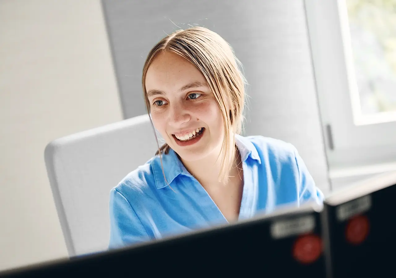 Portraitbild von Mitarbeiterin Frau Rempel an ihrem Arbeitsplatz. lächelnd zur Seite schauend.